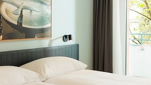 A hotel room with a bed, a wall-mounted light fixture, and a window with curtains.