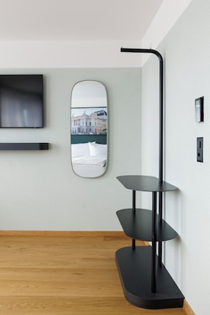 A modern interior with a mounted television, a wall-mounted mirror, and a black metal side table.