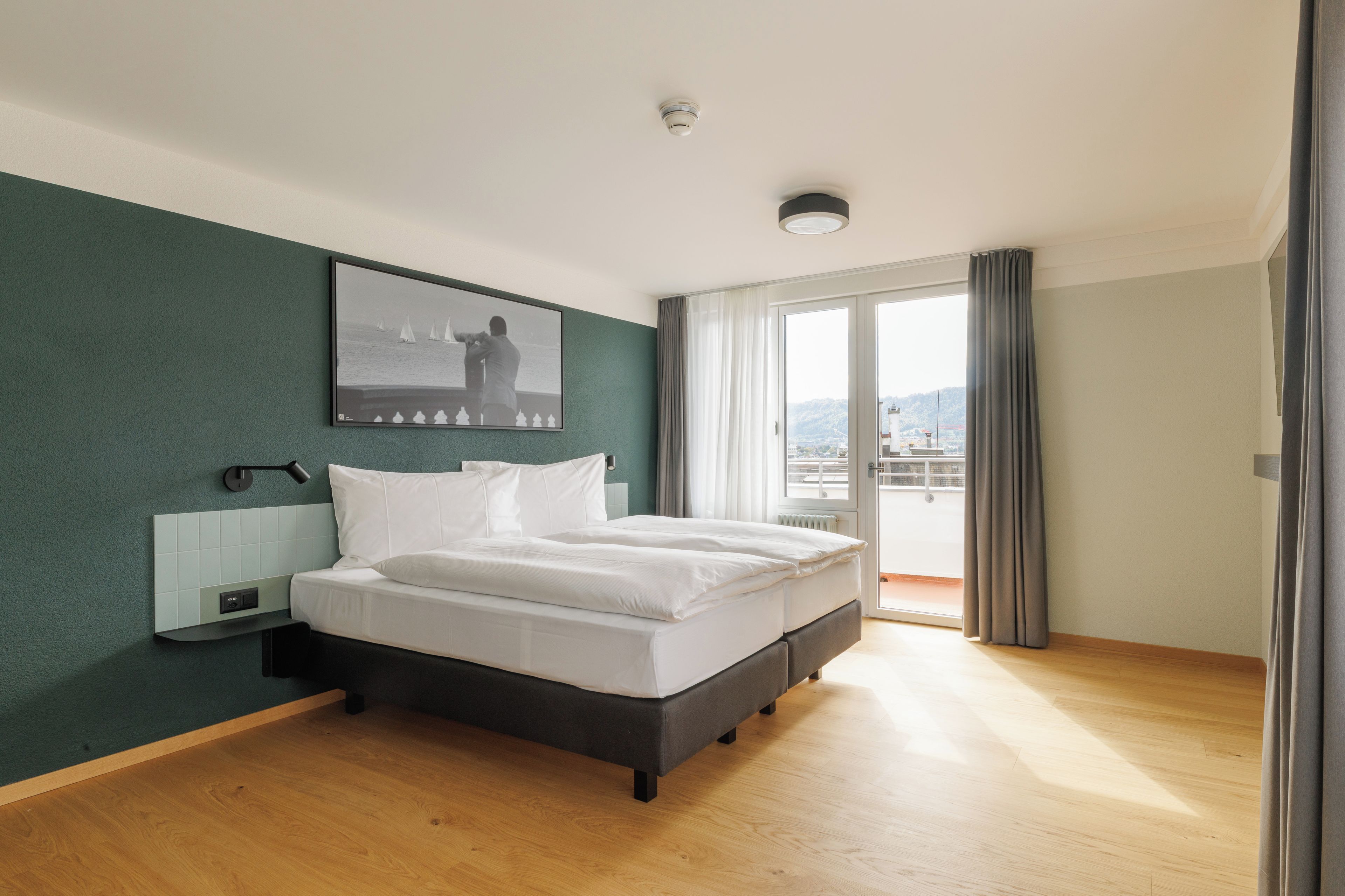Habitación de hotel moderna con una cama grande, vistas de la ciudad a través de la ventana y un cuadro en la pared.