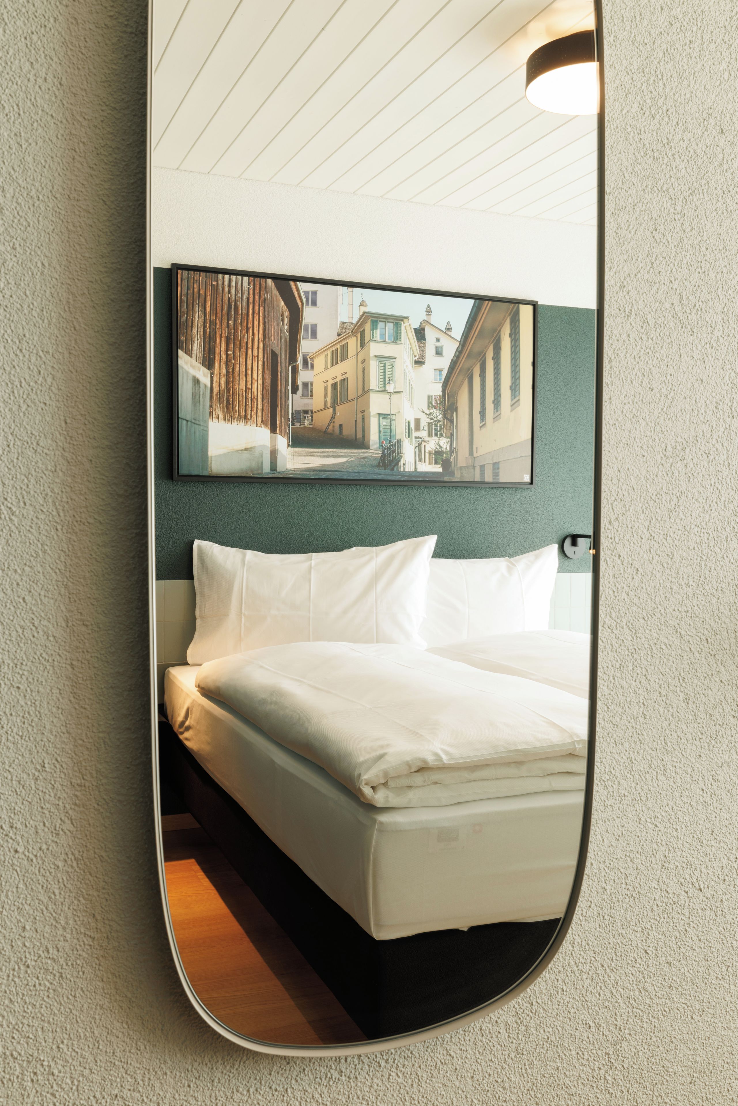 A hotel room with a bed, a large mirror reflecting a city street view, and a ceiling light fixture.