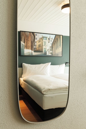 A hotel room with a bed, a large mirror reflecting a city street view, and a ceiling light fixture.