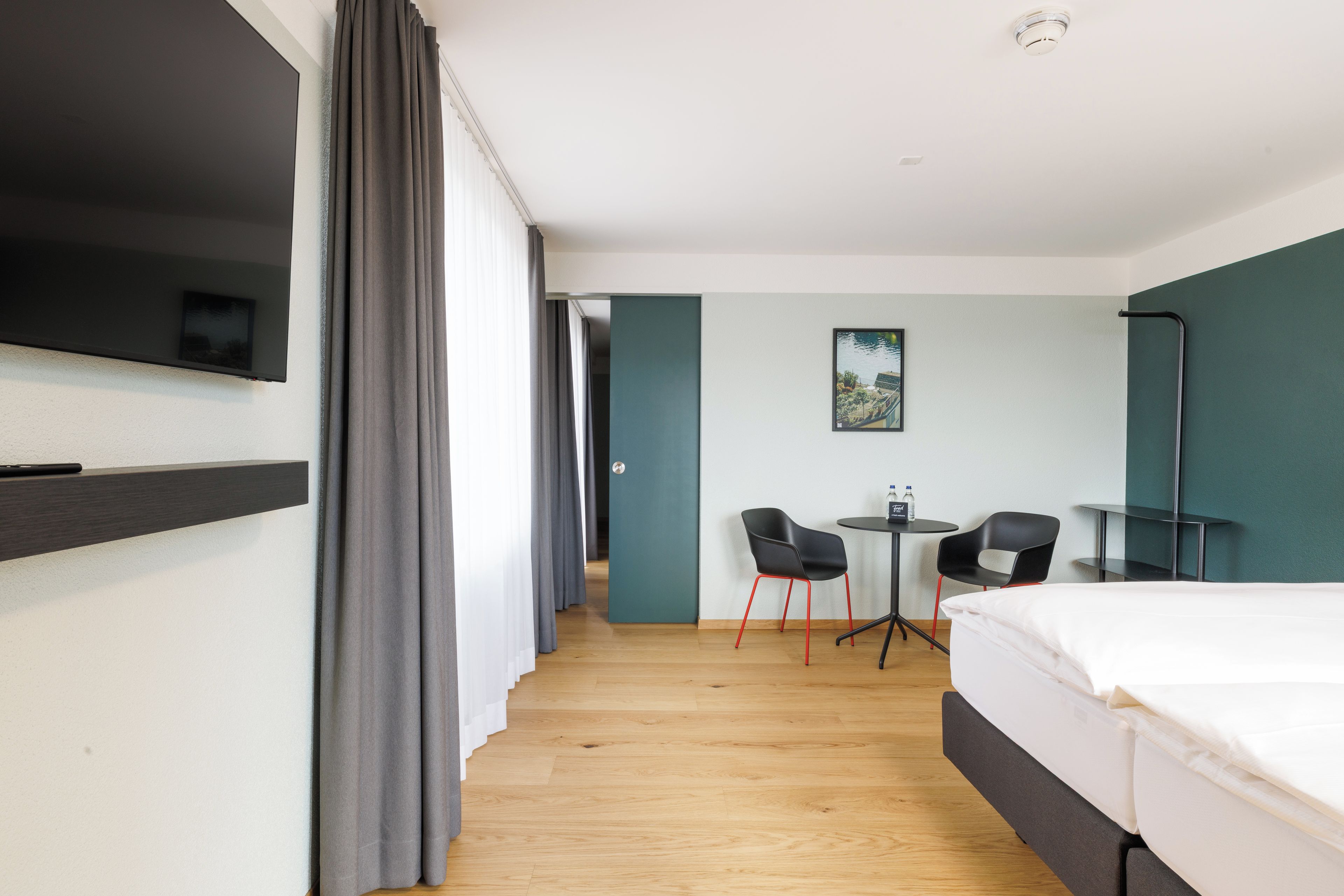 Habitación de hotel con cama, televisión, escritorio y sillas, y un cuadro en la pared.