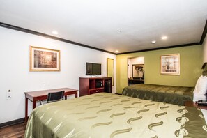 Quarto de hotel com uma cama, escrivaninha, cadeira, televisão e quadros nas paredes.