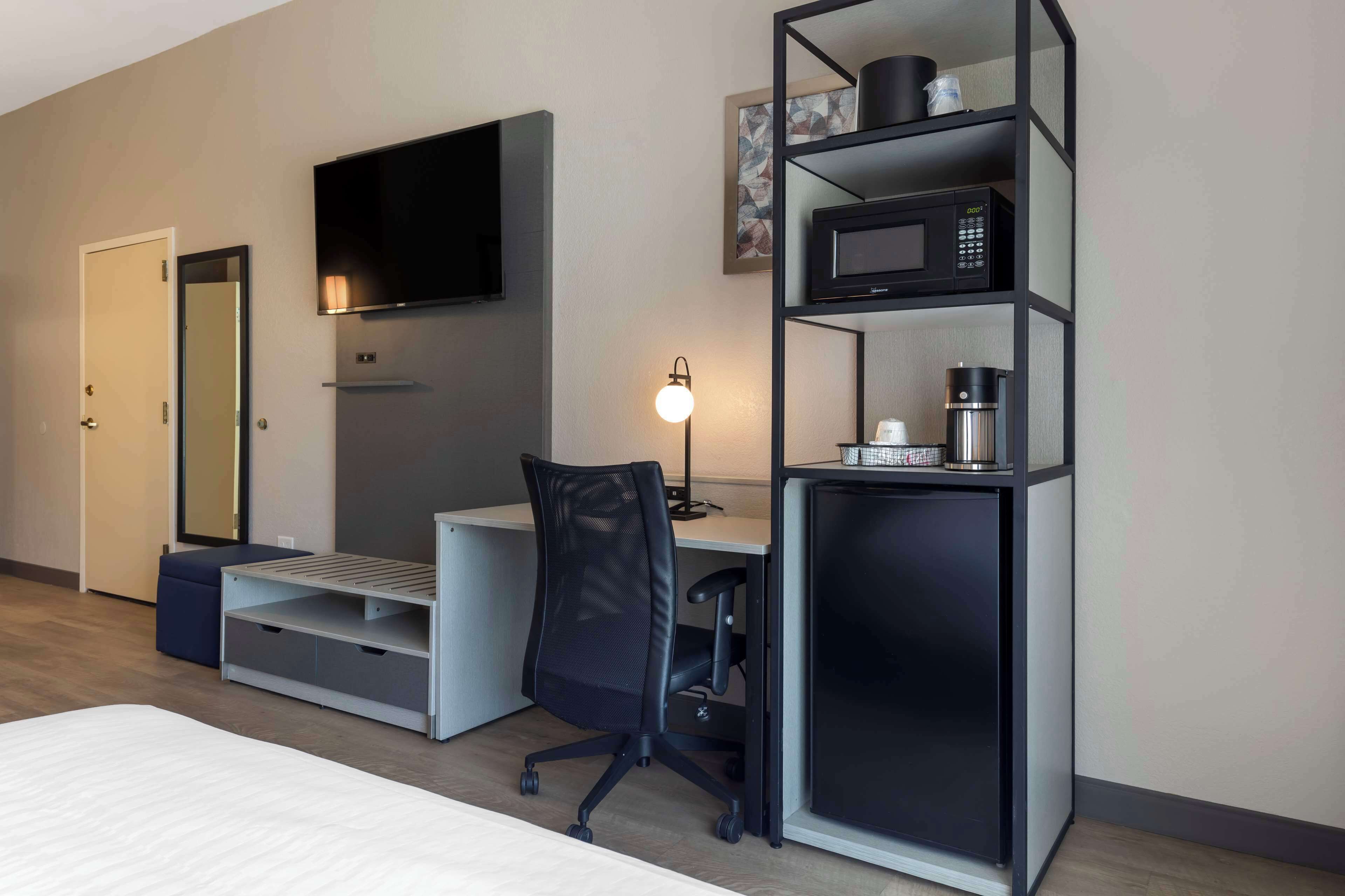 A modern hotel room with a bed, a desk, a chair, a TV, a microwave, and a coffee maker.