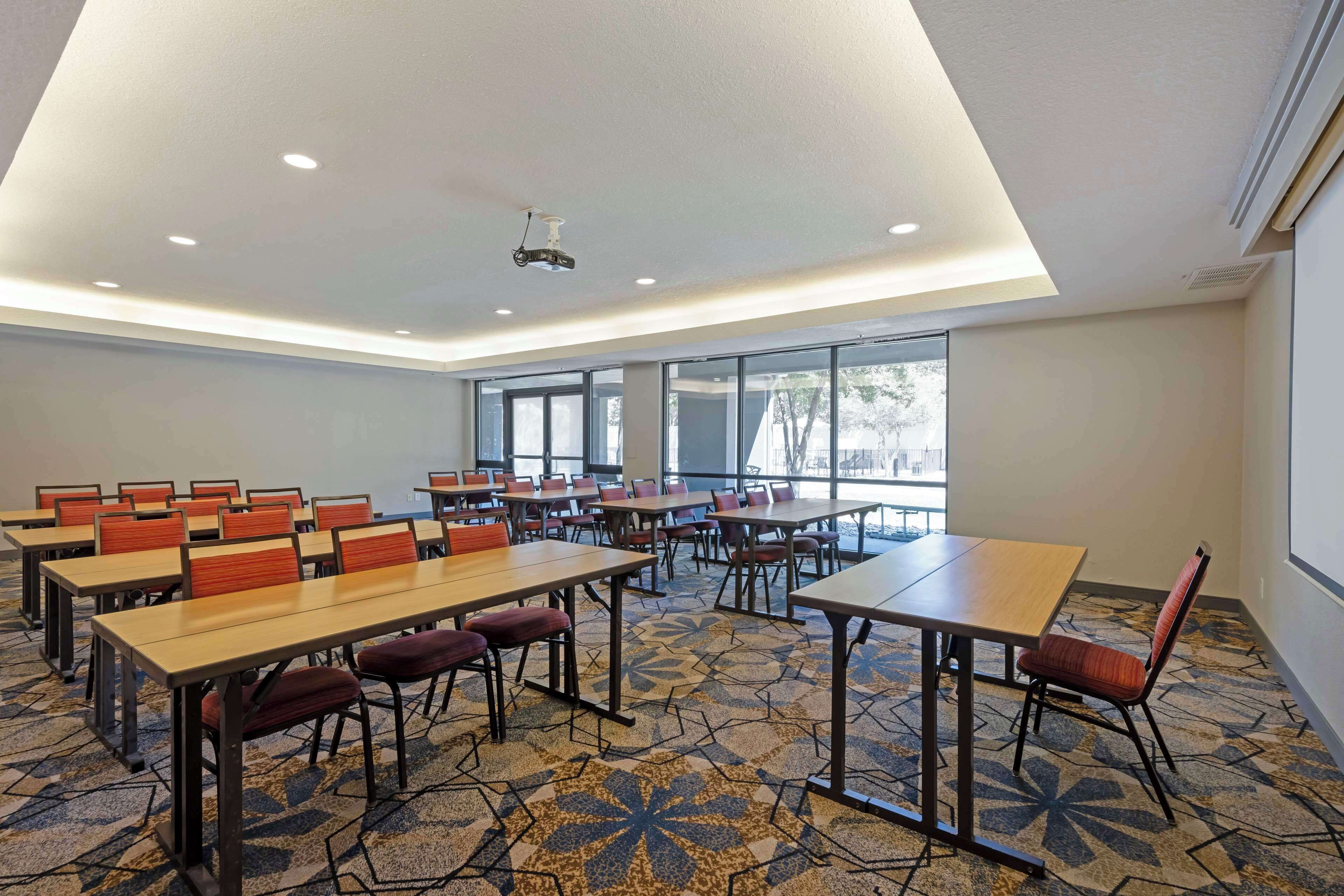 A conference room with tables and chairs, large windows, and a ceiling projector.