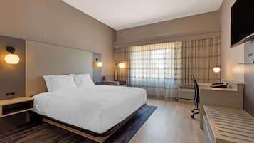 Quarto de hotel moderno com uma cama grande, mesas de cabeceira, uma escrivaninha e uma televisão.