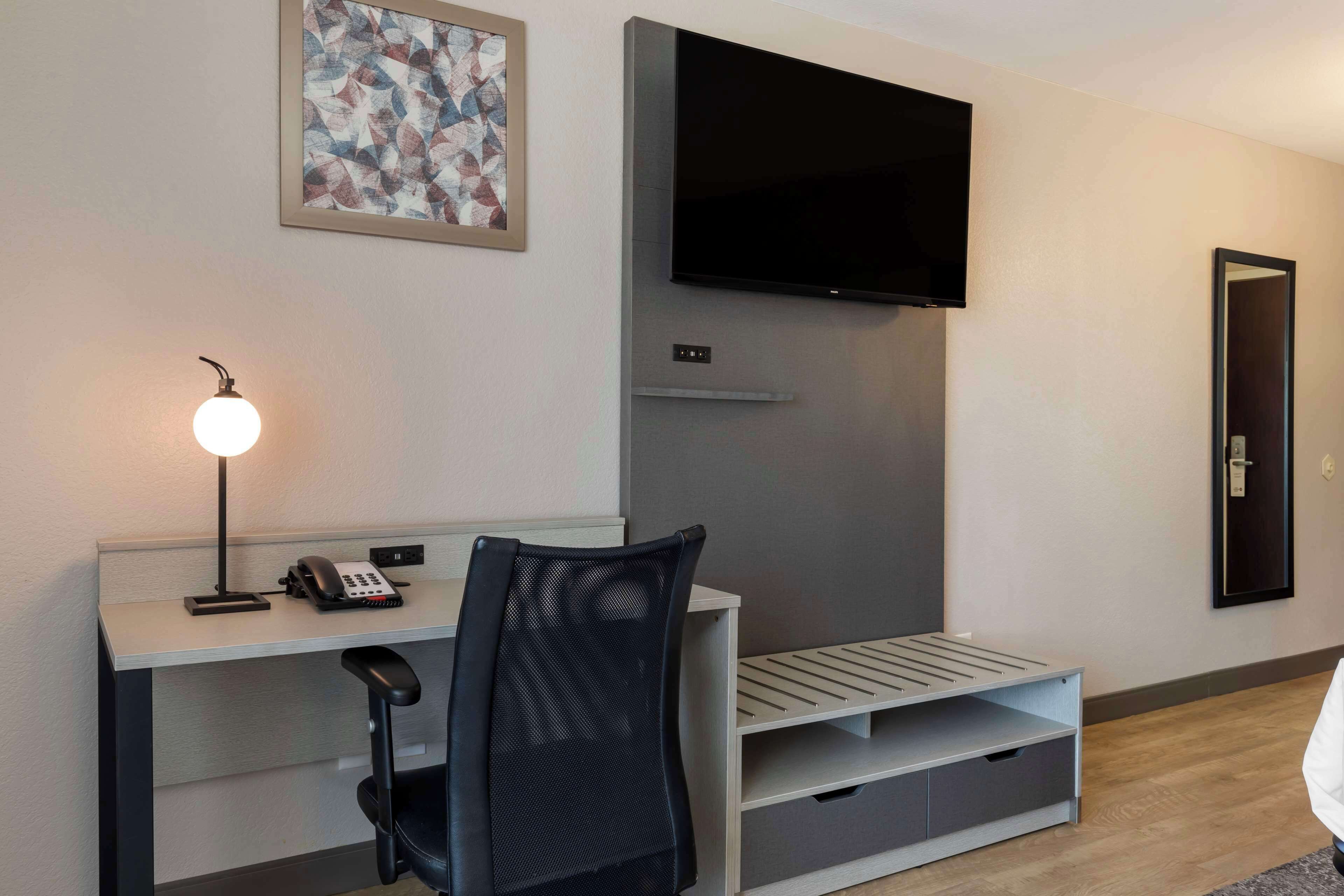 A modern hotel room with a desk, chair, flat-screen TV, and artwork on the wall.