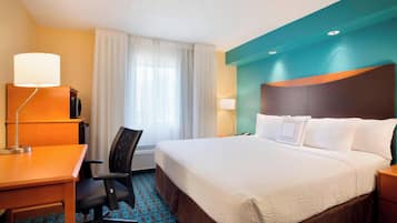 A hotel room with a bed, desk, chair, and a window with curtains.