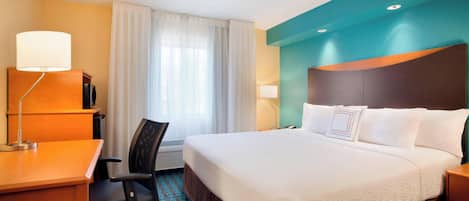 Una habitación de hotel con cama, escritorio, silla y ventana con cortinas.