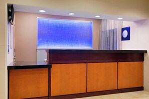 A reception area with a wooden reception desk, a large blue abstract window, and a wall-mounted clock. - Fairfield Inn & Suites Fort Worth University Drive (Fort Worth)