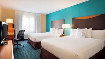 A hotel room with two beds, a desk with a TV, a chair, and a window with curtains.