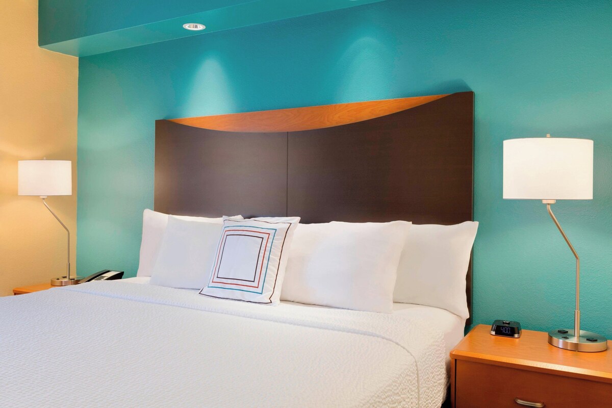 A neatly made bed with white linens, a modern headboard, and two bedside lamps.