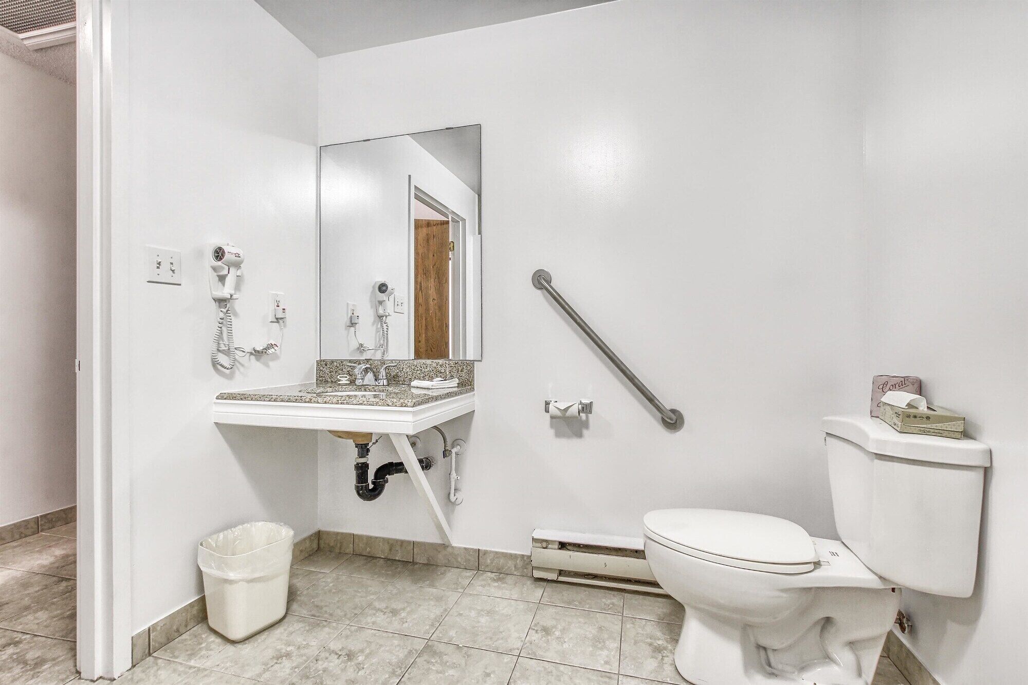 Une salle de bain avec un lavabo blanc, un miroir, des toilettes et une barre d’appui.