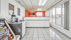 A hotel reception area with a counter, a coffee machine, a waste bin, and a magazine rack. - Motel 6 Windsor, ON (Windsor)