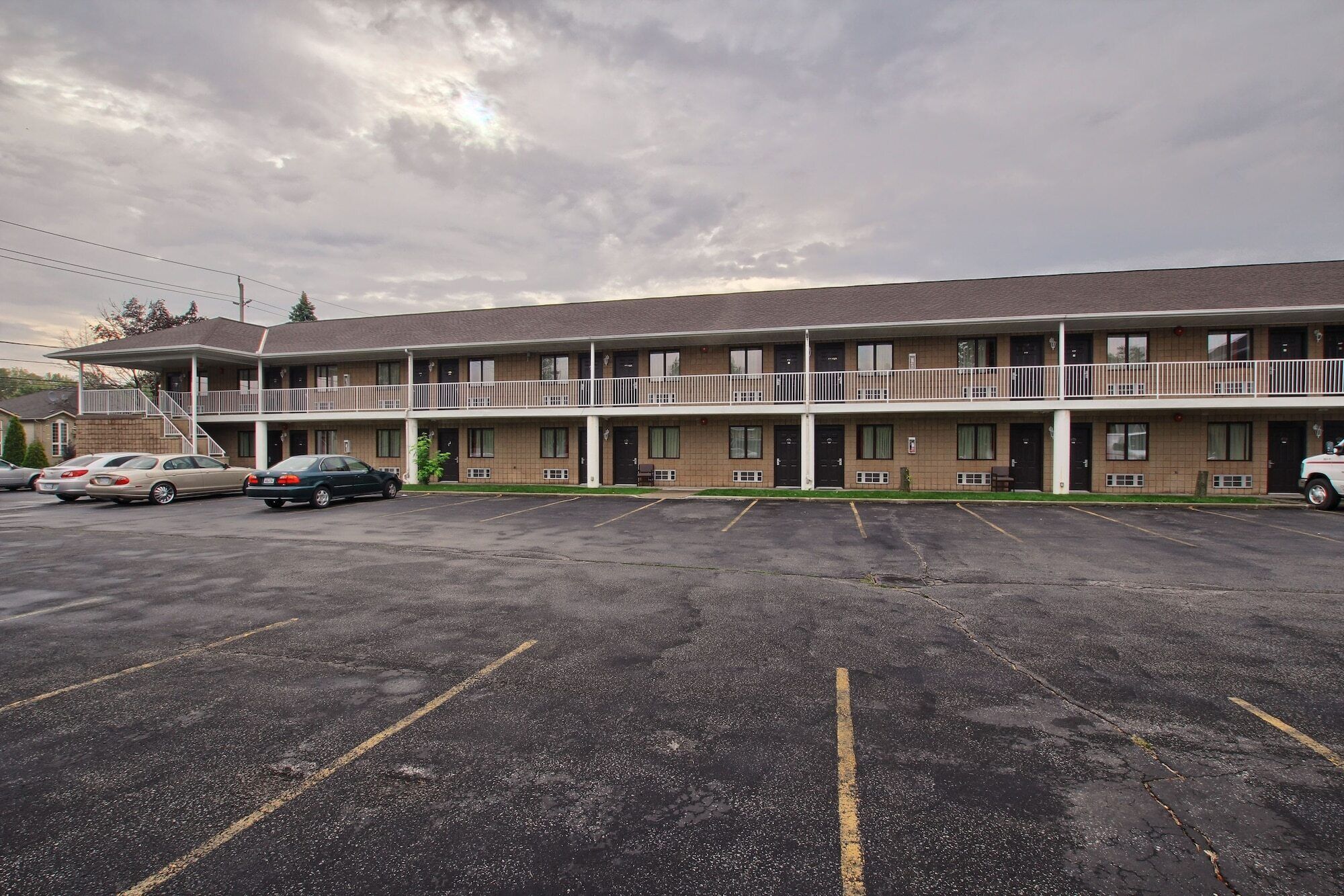 A motel with a two-story structure, a parking lot, and a row of cars parked in front.
