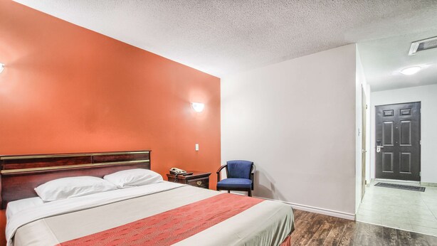 A hotel room with a large bed, a nightstand, a chair, and a door leading to another room. - Motel 6 Windsor, ON (Windsor)