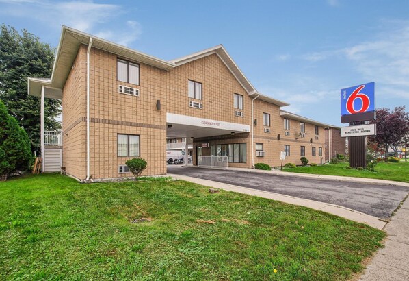 Motel 6 com entrada visível, área de estacionamento coberta e placa indicando WiFi gratuito e quartos renovados.