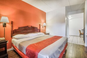 Quarto de hotel com uma cama grande, duas luminárias de cabeceira, uma mesinha de cabeceira e uma cadeira no canto.