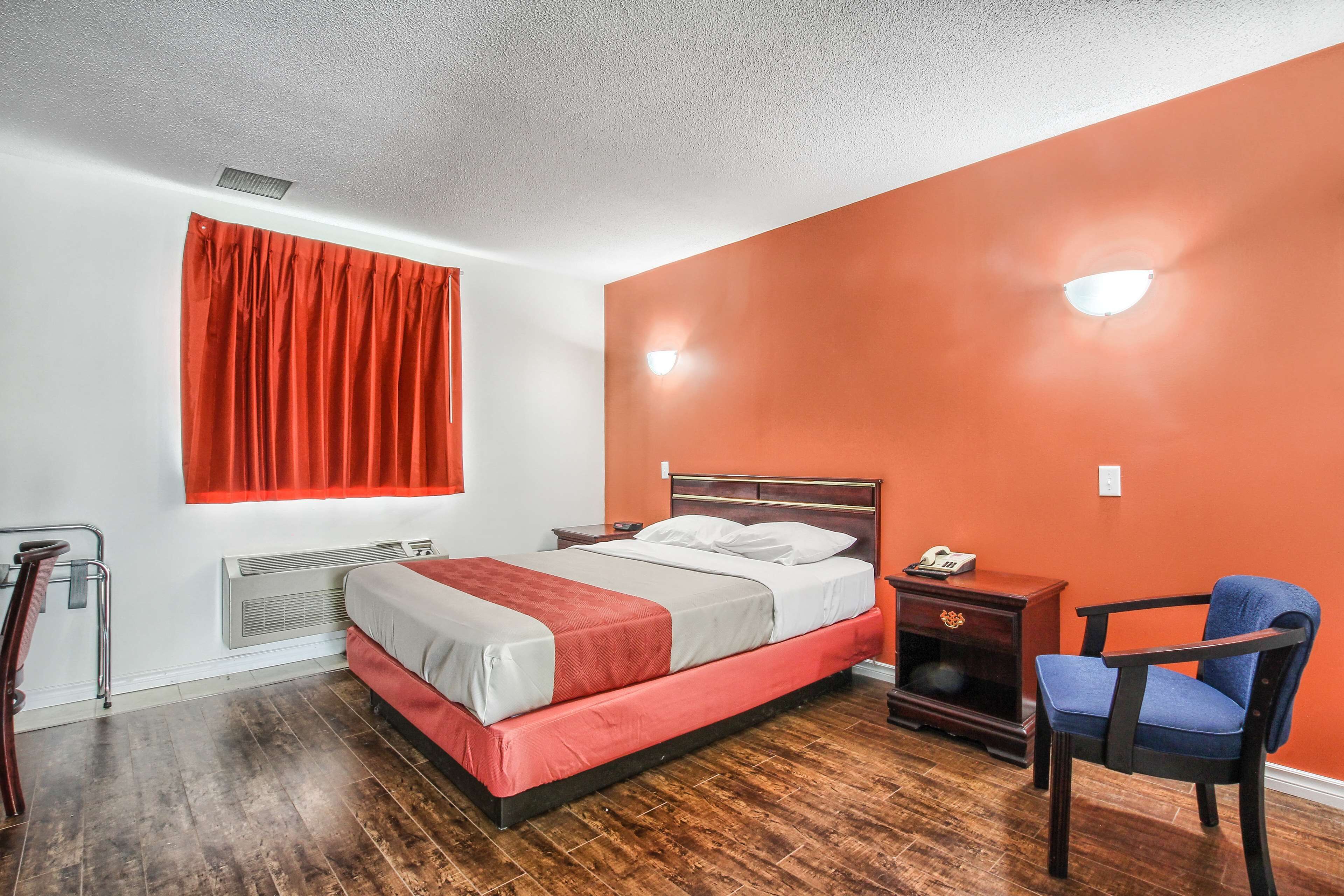 Hotelkamer met een bed, een stoel, een nachtkastje, een verwarming en een raam met rode gordijnen.