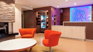 A lobby with orange chairs, a reception desk, a refrigerator stocked with beverages, and a stone wall. - Fairfield Inn & Suites Fort Worth/Fossil Creek (Fort Worth)
