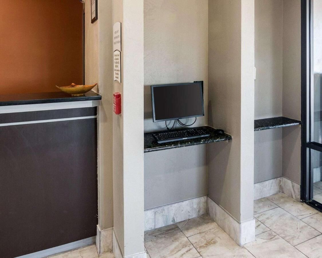 Zona de recepción de un hotel con un mostrador oscuro, un televisor de pantalla plana montado en la pared y un estante pequeño con un teclado.