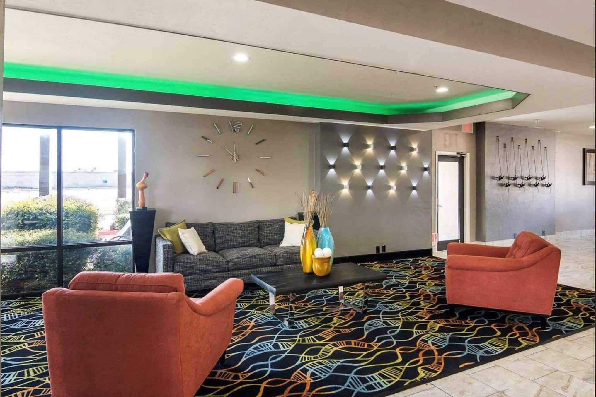 A modern lobby with a large wall clock, a patterned carpet, and two sofas.