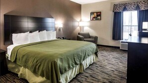Een hotelkamer met een groot bed, twee bedlampjes, een stoel, een bureau en een raam met gordijnen.