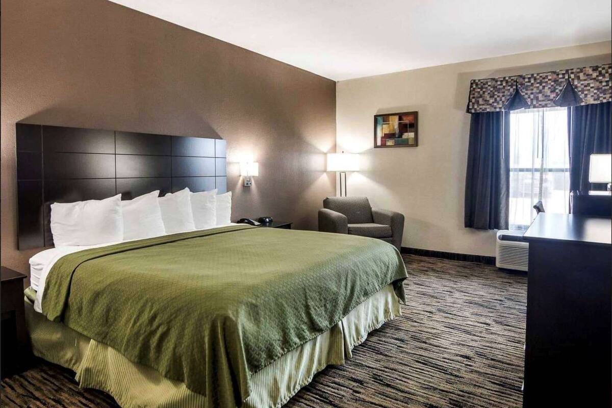 Een hotelkamer met een groot bed, twee bedlampjes, een stoel, een bureau en een raam met gordijnen.