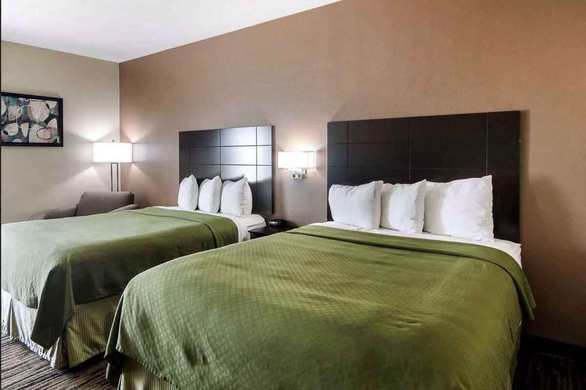 Een hotelkamer met twee bedden, elk met een donker hoofdeinde en witte beddengoed. Aan de linkerkant van de kamer staat een lamp.