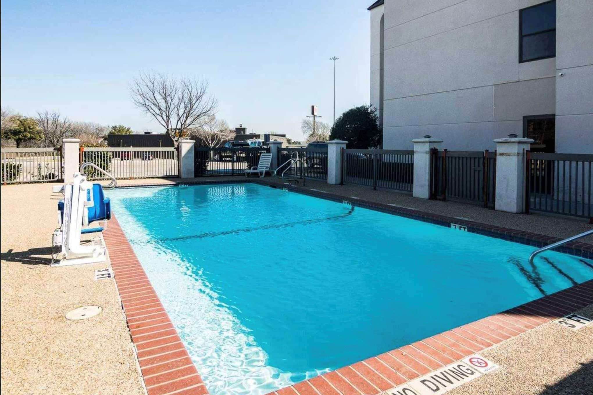 Una piscina con un cartel de buceo, rodeada por una cerca y un edificio.