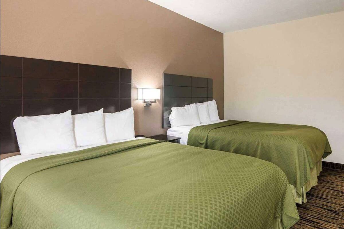 Een hotelkamer met twee bedden, een hoofdeinde, een nachtkastje en een wandlamp.