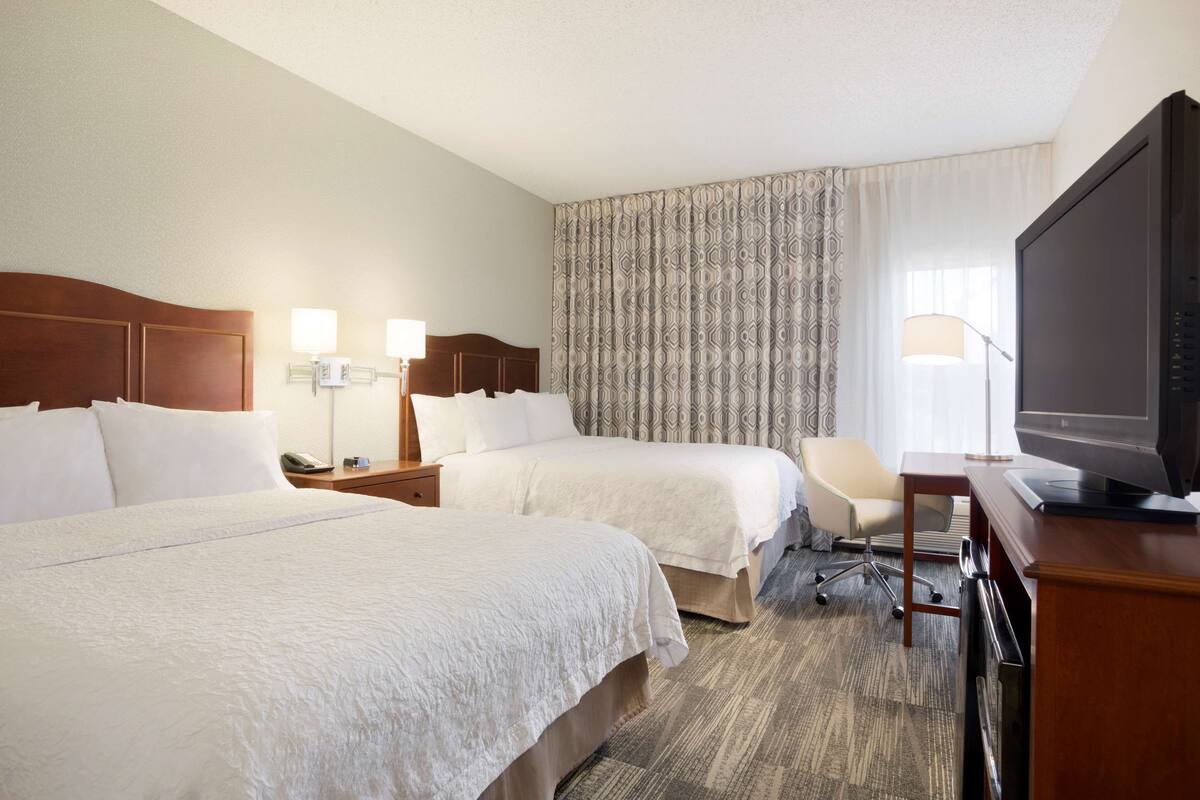 A hotel room with two beds, a desk with a television, and a chair.