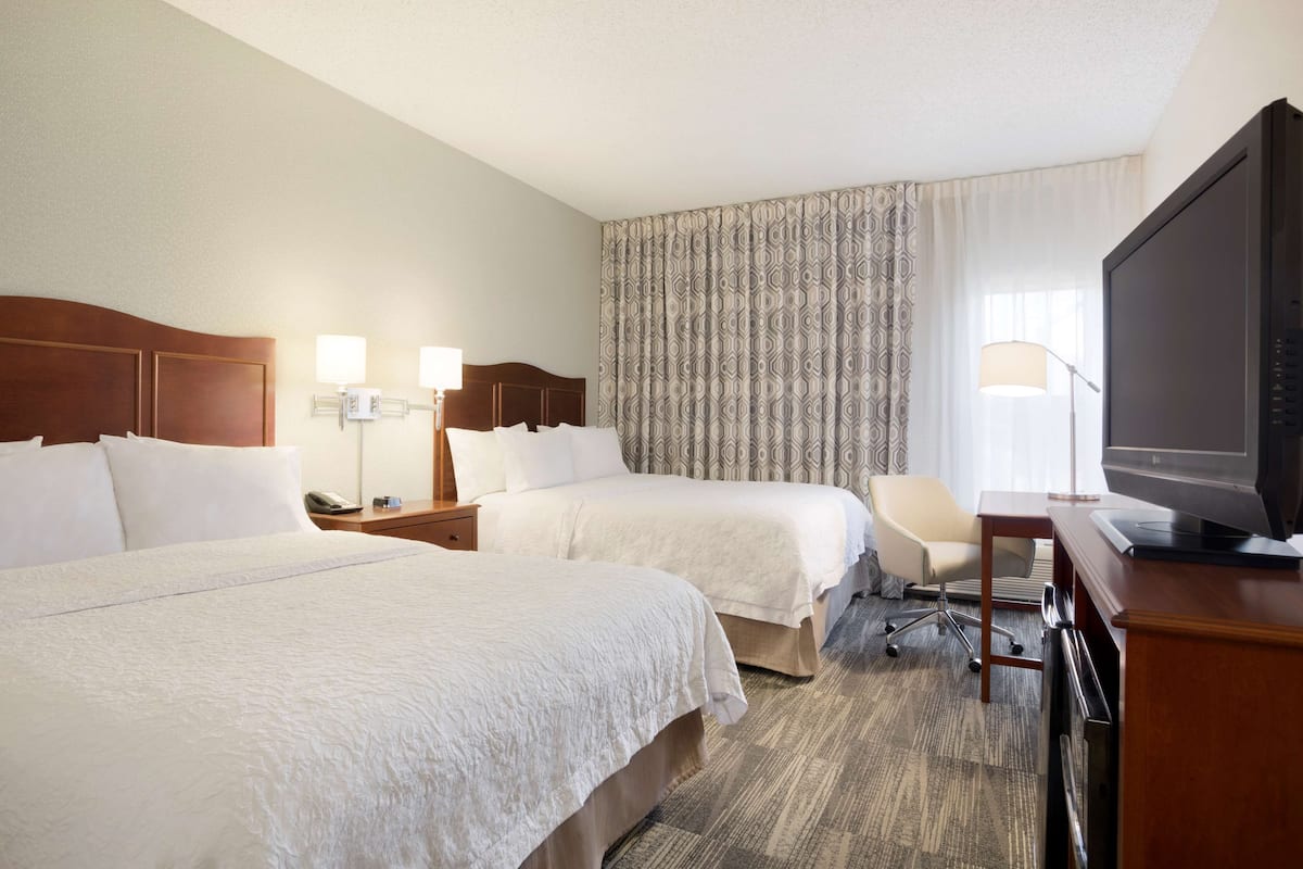 A hotel room with two beds, a desk with a television, and a chair.