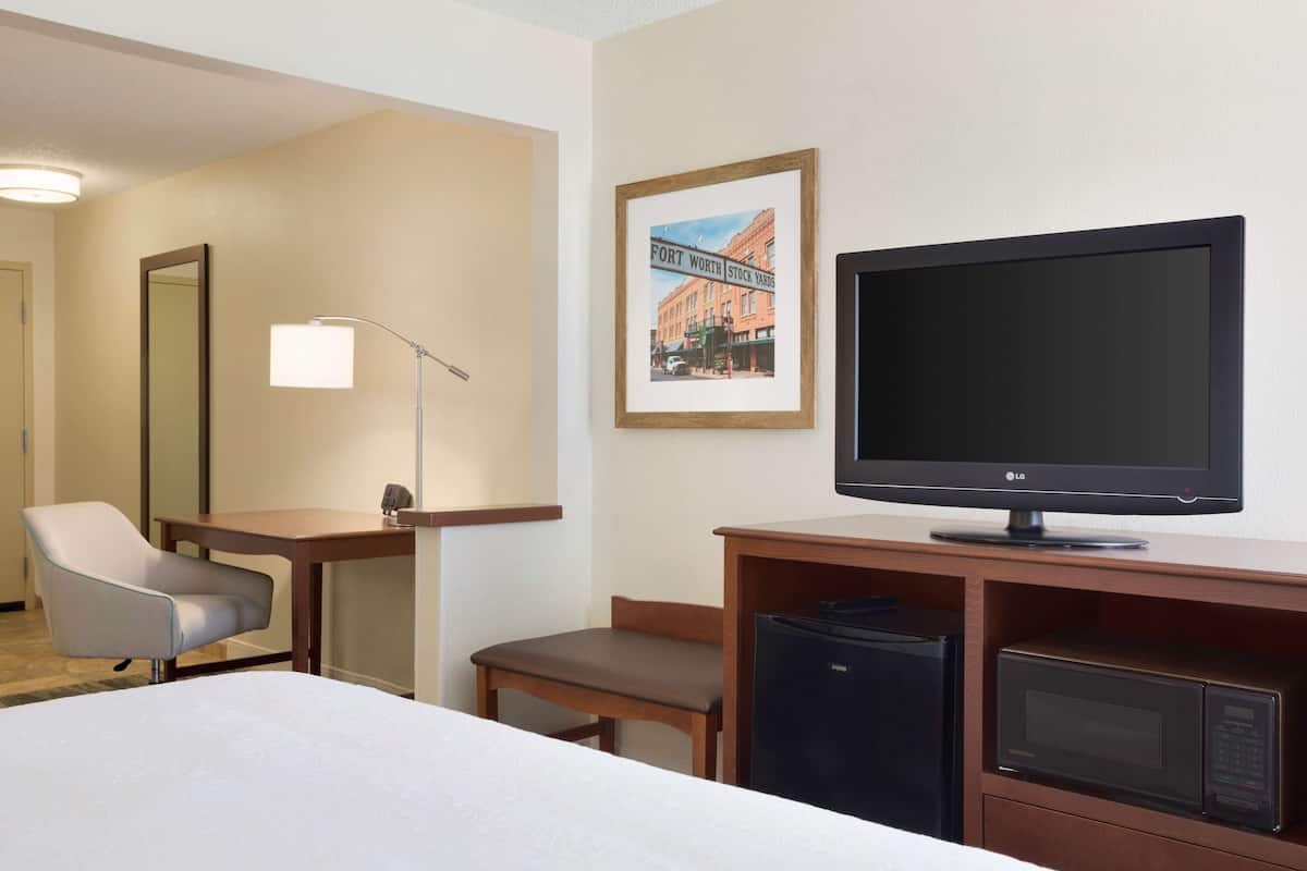 A hotel room with a bed, a desk with a computer, a television, a microwave, and a chair.