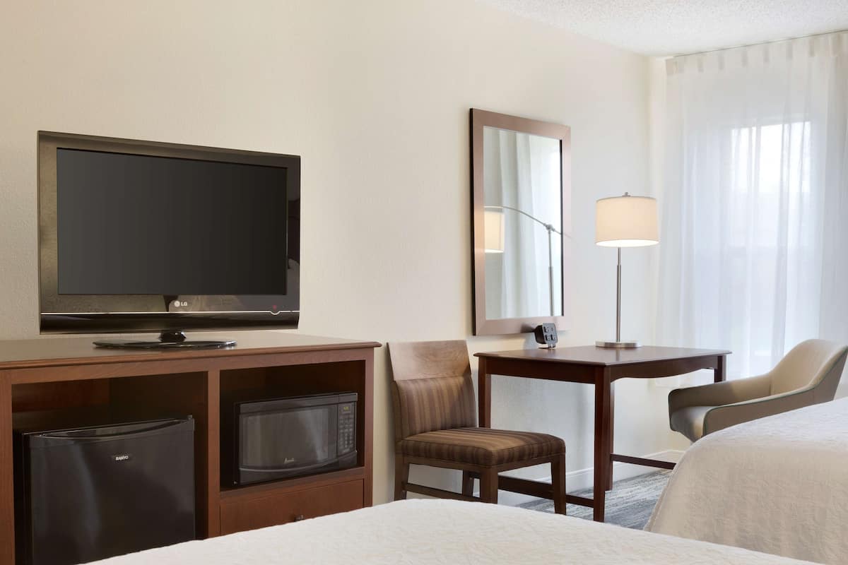 A hotel room with a television, a desk with a lamp, a chair, and a bed.