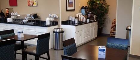 A hotel dining area with tables and chairs, a coffee station, and a trash can.