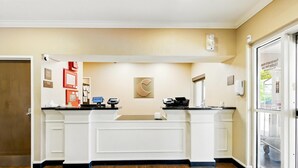 A reception desk with a computer, a telephone, and a coffee machine. There is a door on the left and a glass door on the right. - Comfort Inn South Tulsa - Woodland Hills (Tulsa)