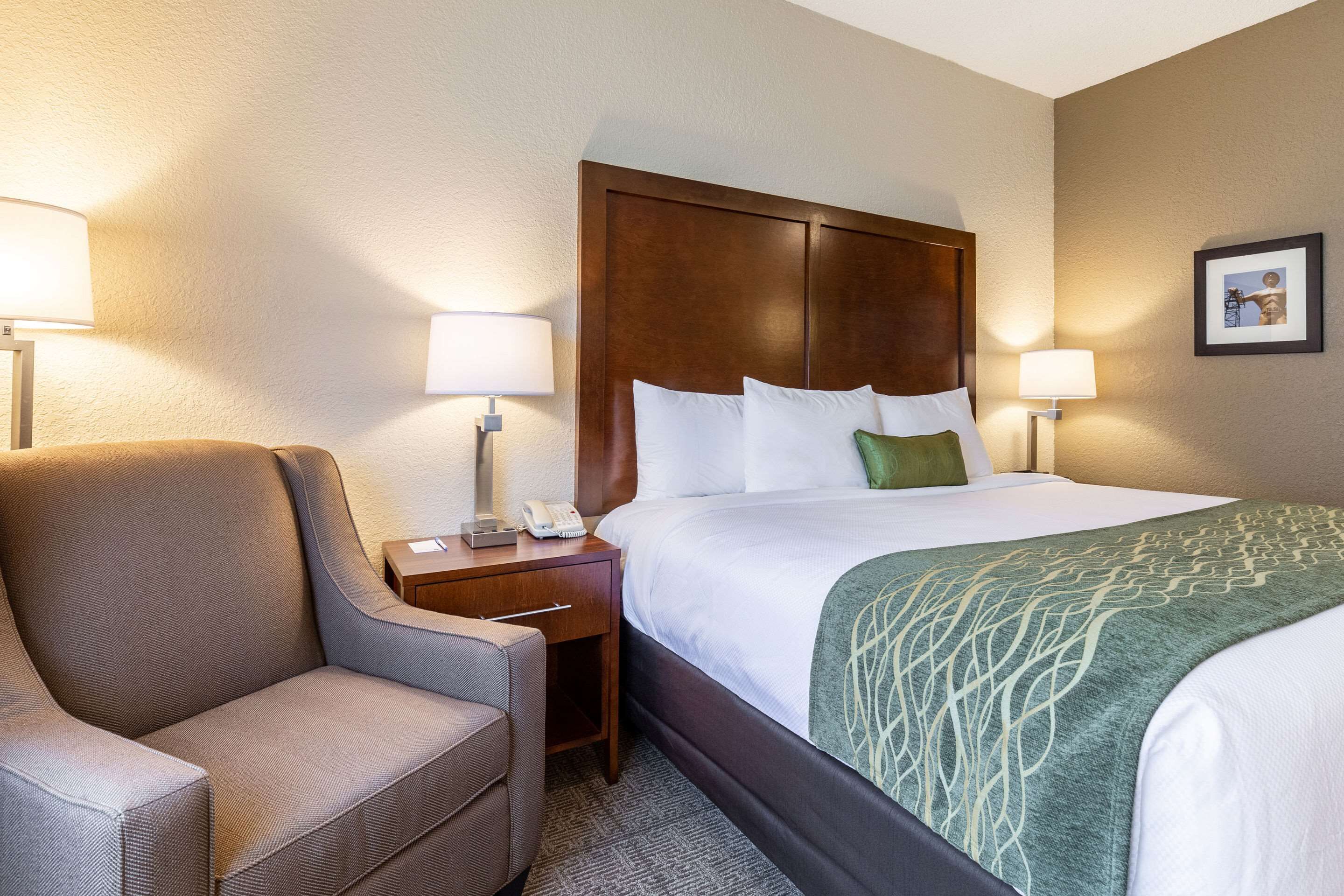 A hotel room with a bed, a chair, a nightstand, and a lamp.