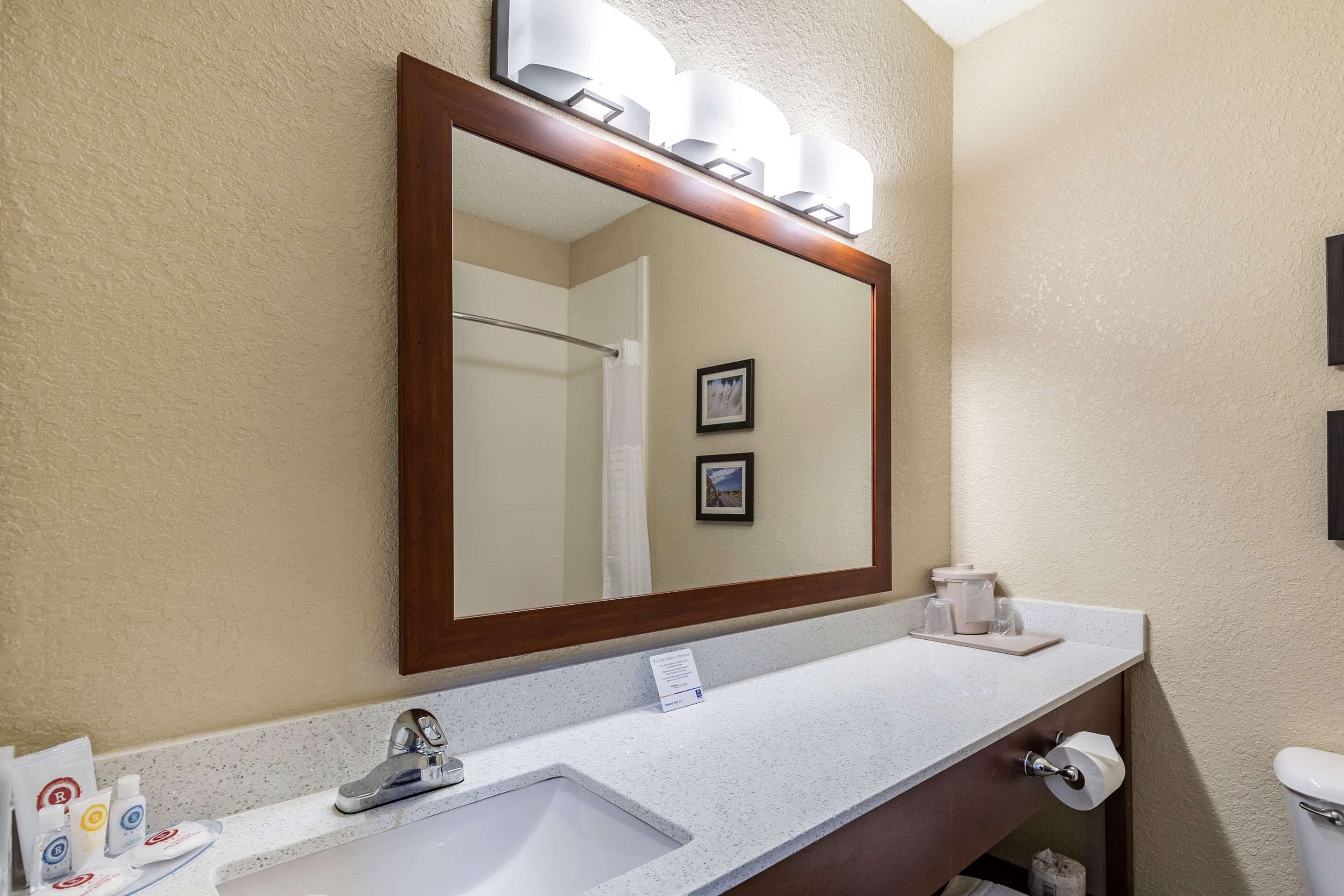 Une salle de bain avec un grand miroir, un lavabo, des toilettes et un porte-serviettes.