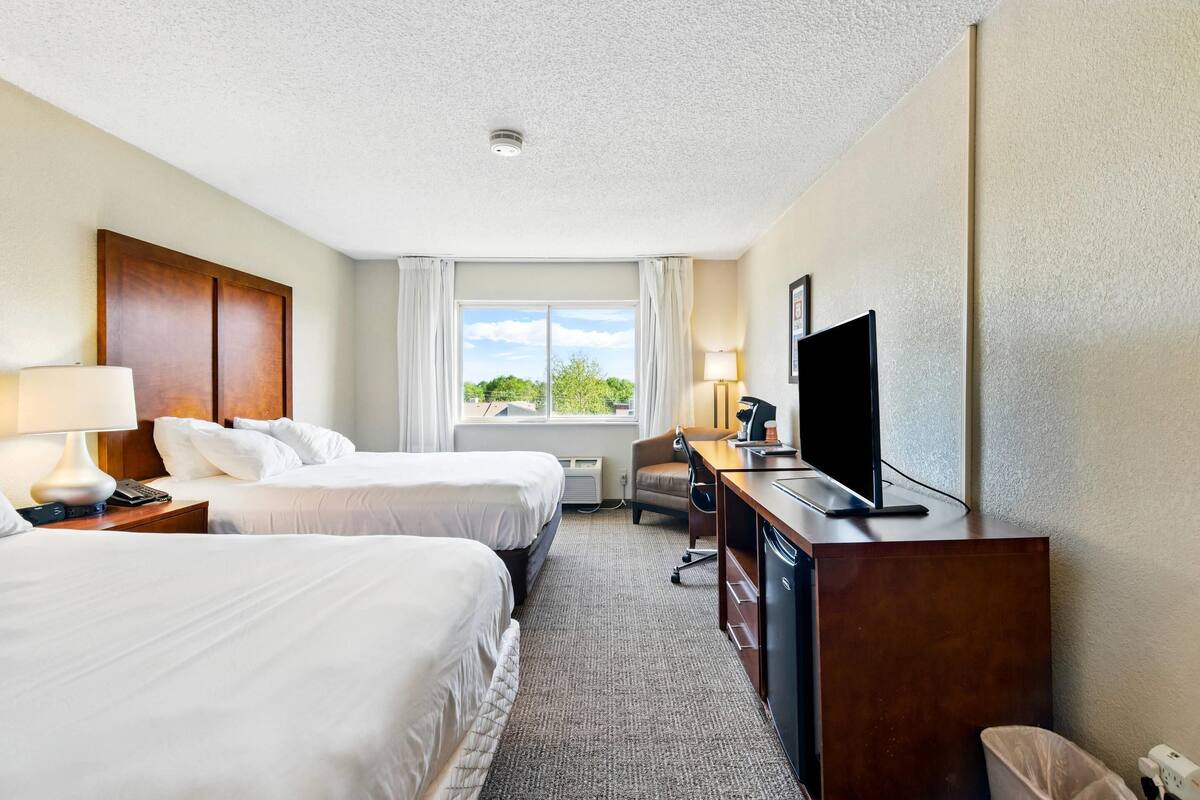 Habitación de hotel con dos camas, un escritorio con televisor, una silla y una ventana con cortinas.