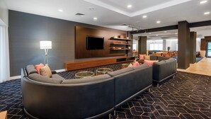 A modern living room with a curved sectional sofa, a flat-screen TV, and a coffee table. - Courtyard by Marriott Columbus Airport (Columbus)