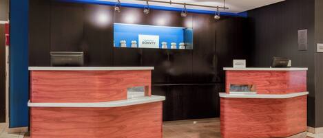 A reception area with two wooden reception desks, a blue wall with a sign, and a modern ceiling design.