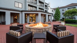 A courtyard with a fire pit surrounded by wicker furniture and a building with balconies and large windows. - Courtyard by Marriott Columbus Airport (Columbus)
