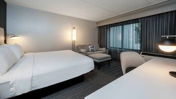 A hotel room with a large bed, a desk, a chair, a sofa, and a lamp.