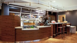 A modern bar area with a wooden counter, a refrigerated display, and a seating area with bar stools. - Courtyard by Marriott Columbus Airport (Columbus)