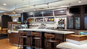 A modern bar area with a curved counter, bar stools, and a coffee machine. - Courtyard by Marriott Columbus Airport (Columbus)