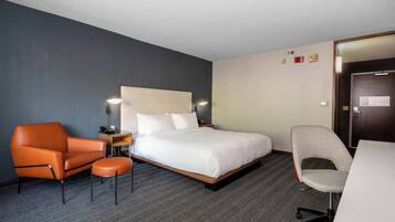 Quarto de hotel com cama, duas cadeiras, escrivaninha e piso coberto de carpete.
