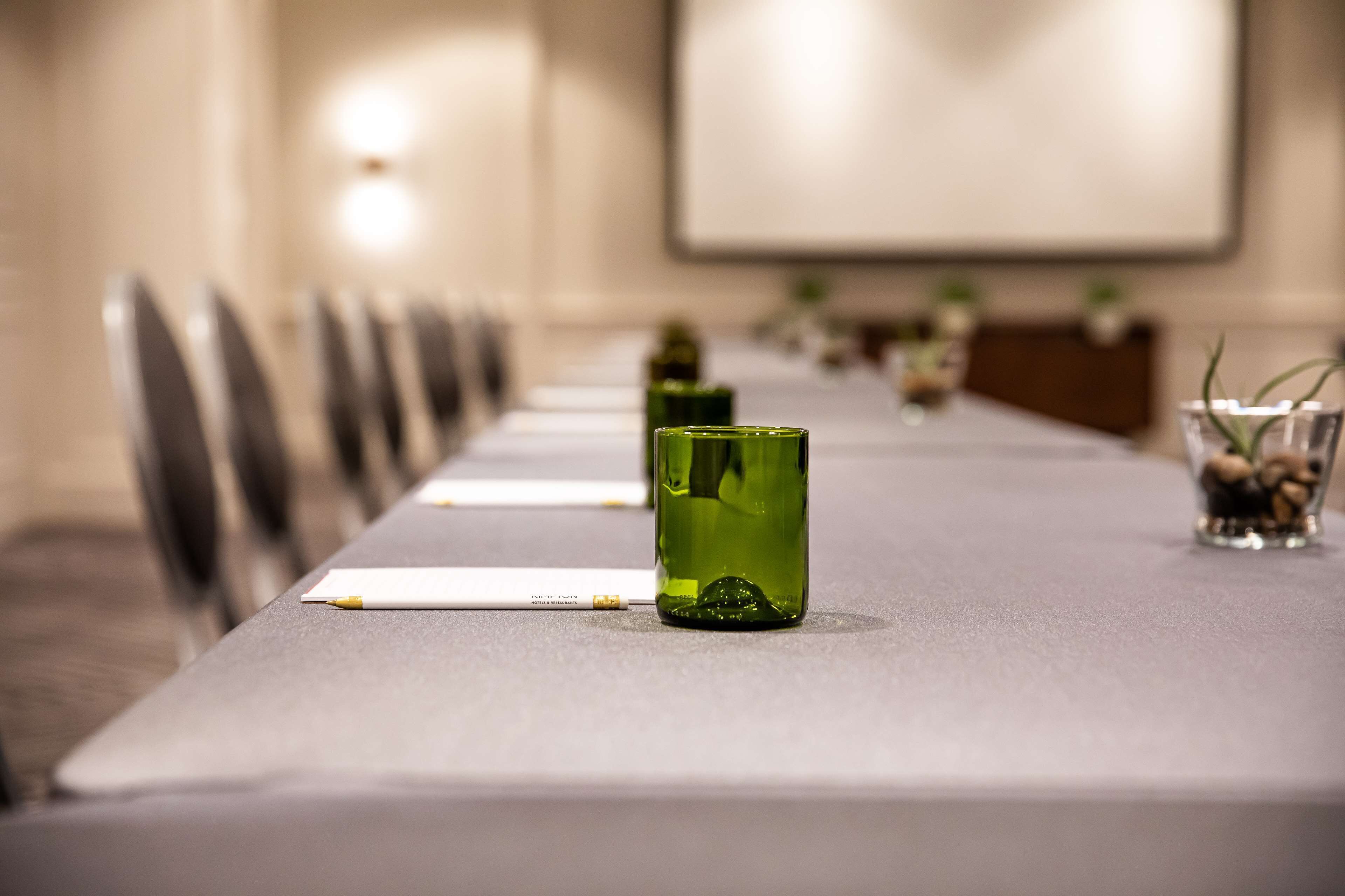 A conference table with chairs, a projector screen, and a row of green glass bottles.