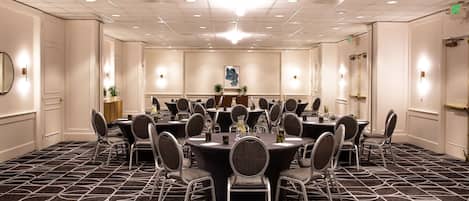 A conference room with multiple round tables and chairs, a chandelier, and a patterned carpet.