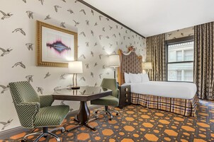 Una habitación de hotel con una cama, dos sillas, una mesa y una lámpara.